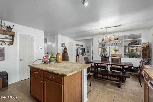 kitchen with light tile patterned floors, a textured ceiling, a center island, and hanging light fixtures