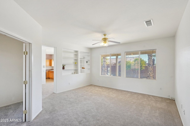 spare room with ceiling fan, built in features, and light carpet