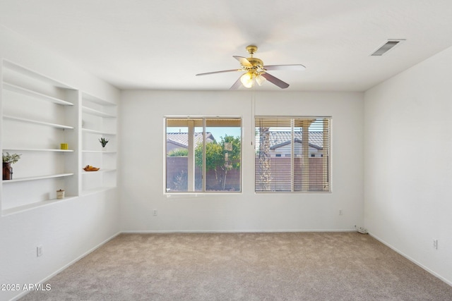 spare room with built in shelves, ceiling fan, and light colored carpet