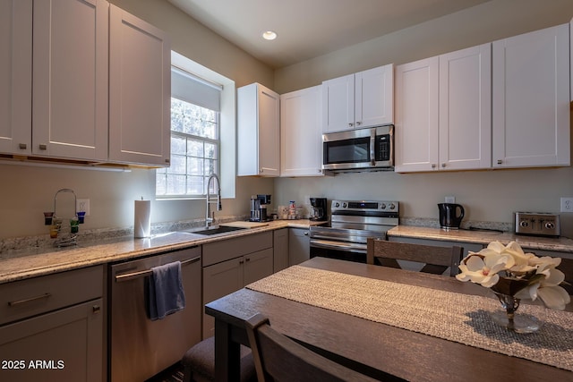 kitchen with a sink, white cabinetry, recessed lighting, light stone countertops, and stainless steel appliances