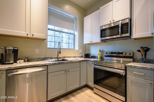 kitchen with light wood-type flooring, a sink, light stone countertops, and stainless steel appliances
