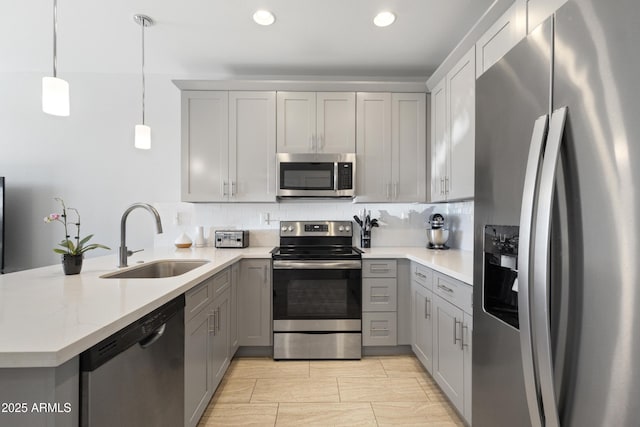 kitchen featuring a peninsula, a sink, backsplash, gray cabinetry, and stainless steel appliances