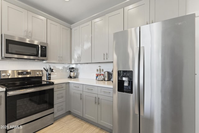 kitchen with light countertops, appliances with stainless steel finishes, gray cabinets, and backsplash