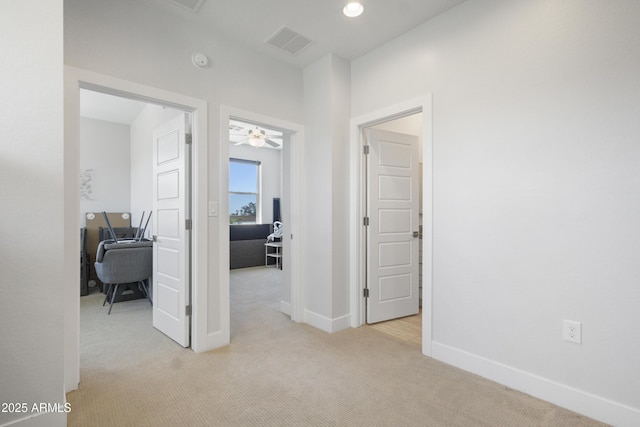 hall with baseboards, visible vents, and light carpet
