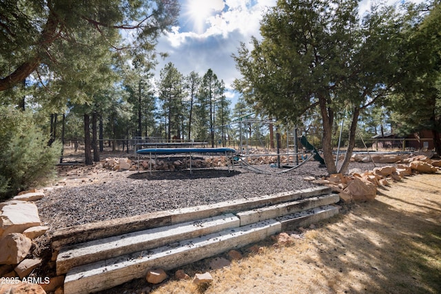 view of yard featuring a trampoline, fence, and playground community