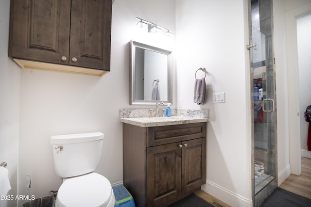 bathroom with vanity, a shower stall, toilet, and baseboards