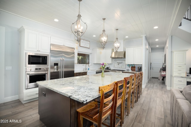 kitchen with backsplash, white cabinetry, a sink, built in appliances, and under cabinet range hood