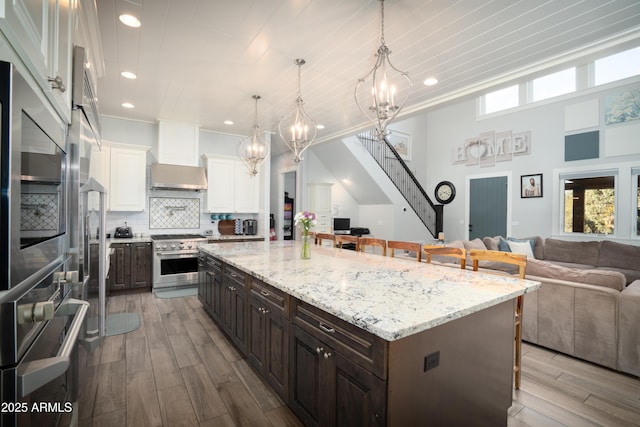 kitchen with wall chimney range hood, a kitchen breakfast bar, stainless steel appliances, and open floor plan