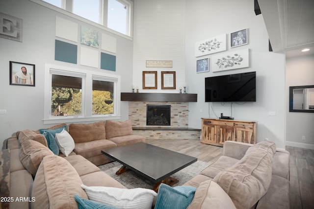 living room featuring a fireplace, a towering ceiling, baseboards, and wood finished floors