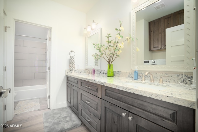 bathroom featuring wood finished floors, a sink, visible vents, tub / shower combination, and double vanity