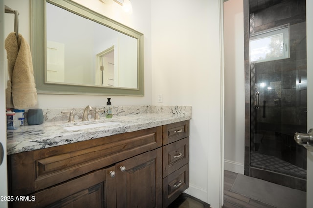 bathroom featuring wood finished floors, a shower stall, vanity, and baseboards