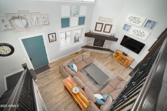 living area with a high ceiling, baseboards, wood finished floors, and a stone fireplace