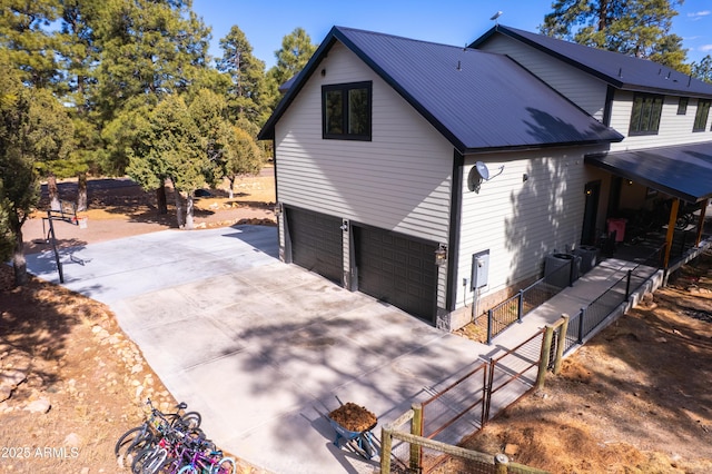 exterior space featuring a garage, metal roof, driveway, and fence