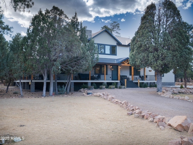 view of front of home with metal roof, driveway, a porch, and a chimney