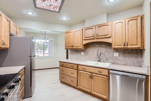 kitchen with appliances with stainless steel finishes, a sink, light brown cabinetry, light wood-style floors, and backsplash