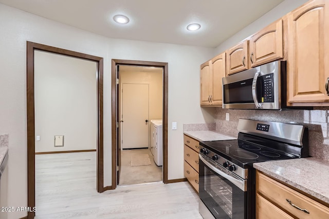 kitchen featuring light wood-style flooring, backsplash, light brown cabinetry, appliances with stainless steel finishes, and washing machine and dryer