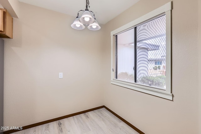 spare room with a notable chandelier, light wood-type flooring, and baseboards