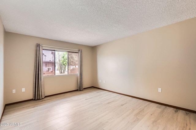 spare room with a textured ceiling, light wood-style flooring, and baseboards