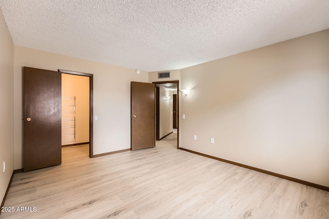 unfurnished bedroom with light wood-style floors, visible vents, baseboards, and a textured ceiling