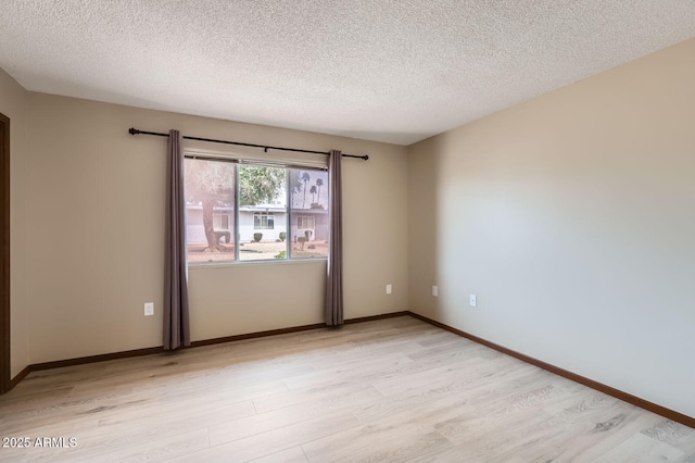 empty room with light wood-style flooring, baseboards, and a textured ceiling