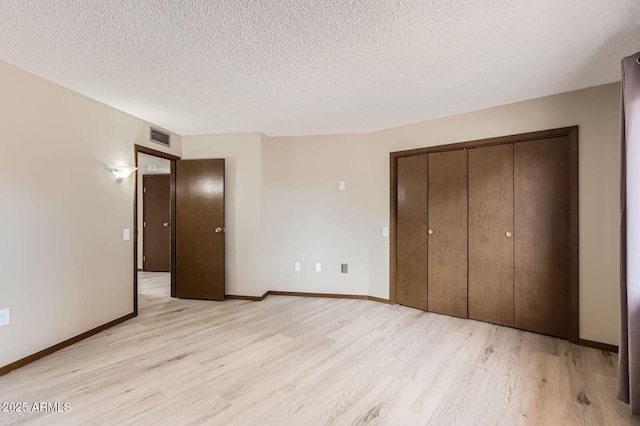 unfurnished bedroom featuring a textured ceiling, light wood-style flooring, visible vents, baseboards, and a closet