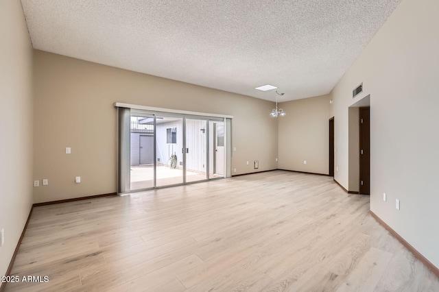 spare room with a chandelier, a textured ceiling, visible vents, baseboards, and light wood-style floors