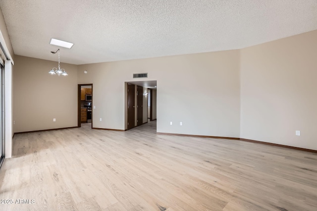 spare room featuring light wood finished floors, visible vents, an inviting chandelier, a textured ceiling, and baseboards