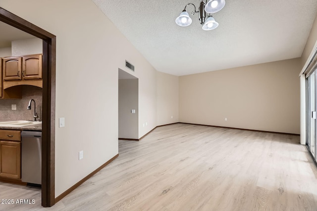 interior space with light wood finished floors, visible vents, a sink, a textured ceiling, and baseboards