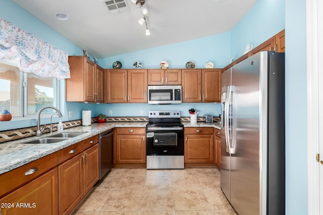 kitchen with sink, vaulted ceiling, appliances with stainless steel finishes, light tile patterned flooring, and light stone counters