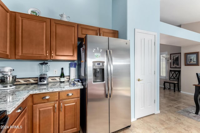 kitchen with stainless steel fridge, light stone counters, and light tile patterned flooring