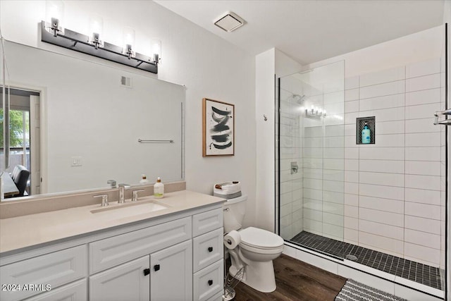 bathroom with tiled shower, vanity, wood-type flooring, and toilet