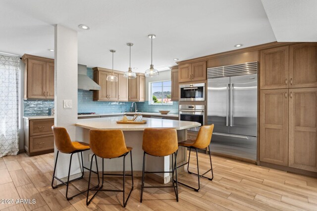 14802 N 3rd Ave, Phoenix, AZ 85023 - kitchen featuring light wood-style floors, wall chimney range hood, light countertops, brown cabinets, and appliances with stainless steel finishes