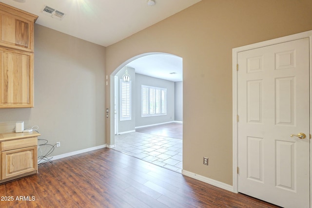 empty room with visible vents, arched walkways, baseboards, and dark wood finished floors