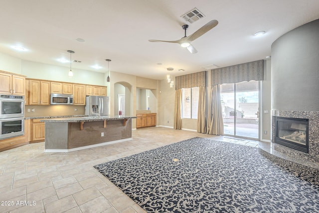 kitchen with light stone countertops, visible vents, a high end fireplace, appliances with stainless steel finishes, and a kitchen breakfast bar