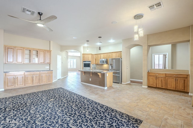 kitchen with stainless steel appliances, arched walkways, visible vents, and a kitchen bar