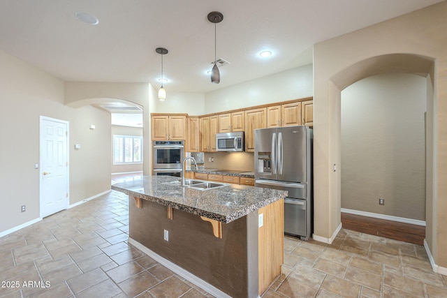 kitchen with a breakfast bar, an island with sink, arched walkways, stainless steel appliances, and a sink