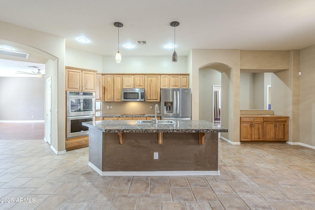 kitchen featuring visible vents, dark stone counters, appliances with stainless steel finishes, arched walkways, and a sink