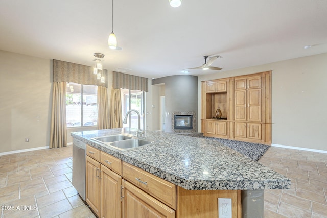 kitchen with baseboards, dishwasher, a glass covered fireplace, stone finish floor, and a sink