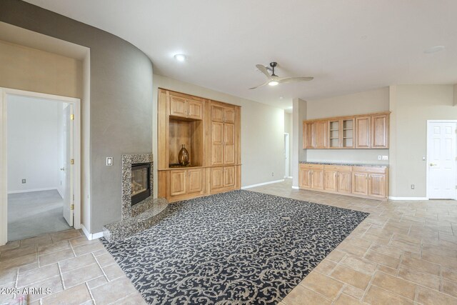 living room featuring a premium fireplace, baseboards, ceiling fan, and stone finish floor