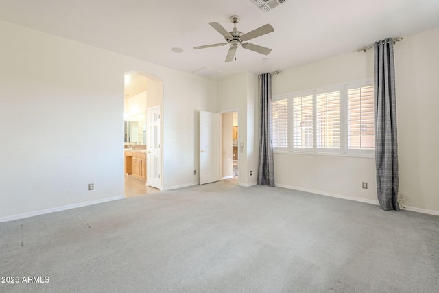 unfurnished bedroom featuring visible vents, light carpet, connected bathroom, arched walkways, and baseboards