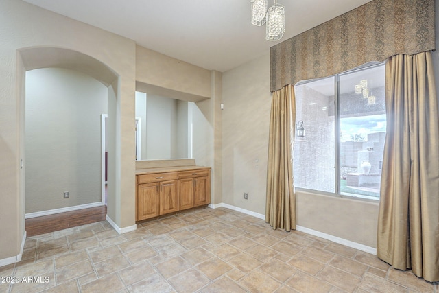 unfurnished room featuring arched walkways, stone finish flooring, and baseboards