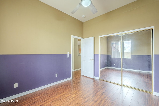 unfurnished bedroom featuring a closet, baseboards, wood finished floors, and a ceiling fan