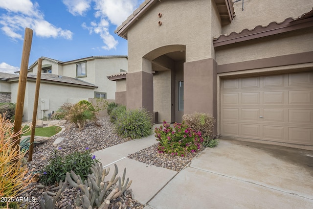 entrance to property featuring stucco siding, a garage, concrete driveway, and a tiled roof