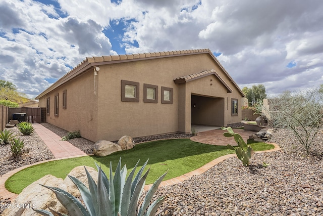 rear view of house with stucco siding, a patio, fence, an attached garage, and a tiled roof