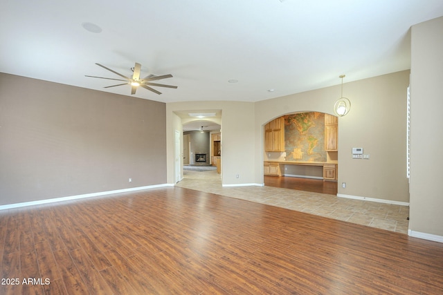 unfurnished living room with a ceiling fan, light wood-type flooring, and baseboards