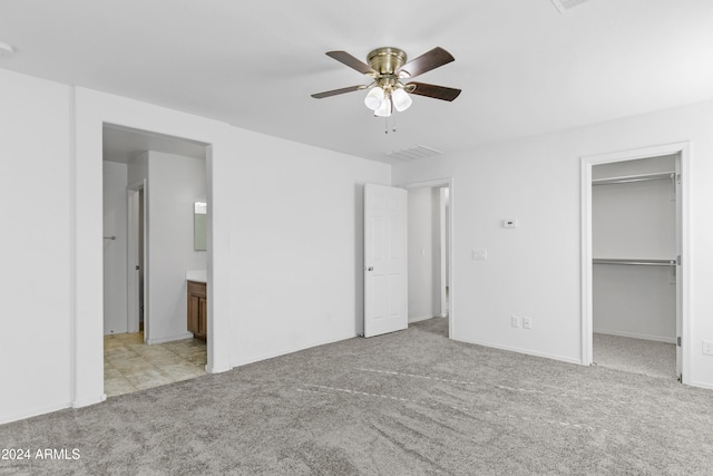 unfurnished bedroom with light colored carpet, a spacious closet, ensuite bath, and ceiling fan