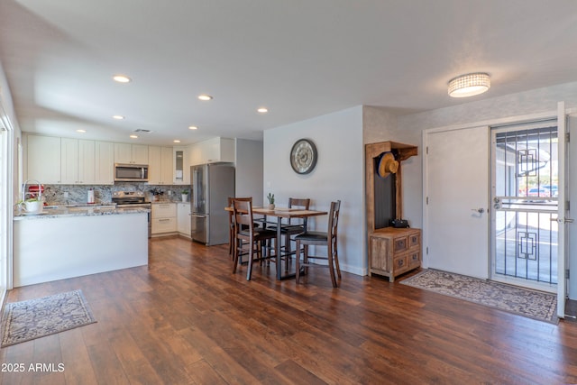 kitchen with light stone counters, dark wood finished floors, appliances with stainless steel finishes, glass insert cabinets, and white cabinetry