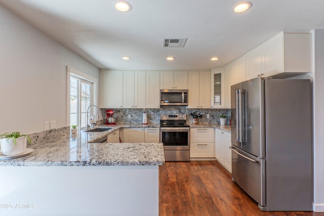 kitchen featuring visible vents, backsplash, appliances with stainless steel finishes, a sink, and light stone countertops