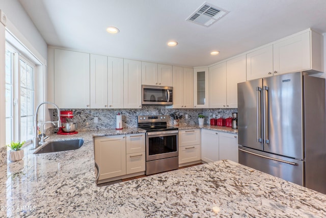 kitchen featuring a sink, visible vents, appliances with stainless steel finishes, backsplash, and glass insert cabinets