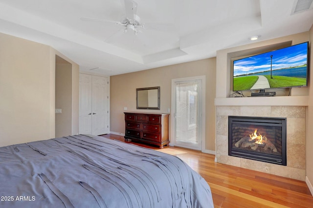 bedroom with a raised ceiling, visible vents, a tiled fireplace, a ceiling fan, and wood finished floors